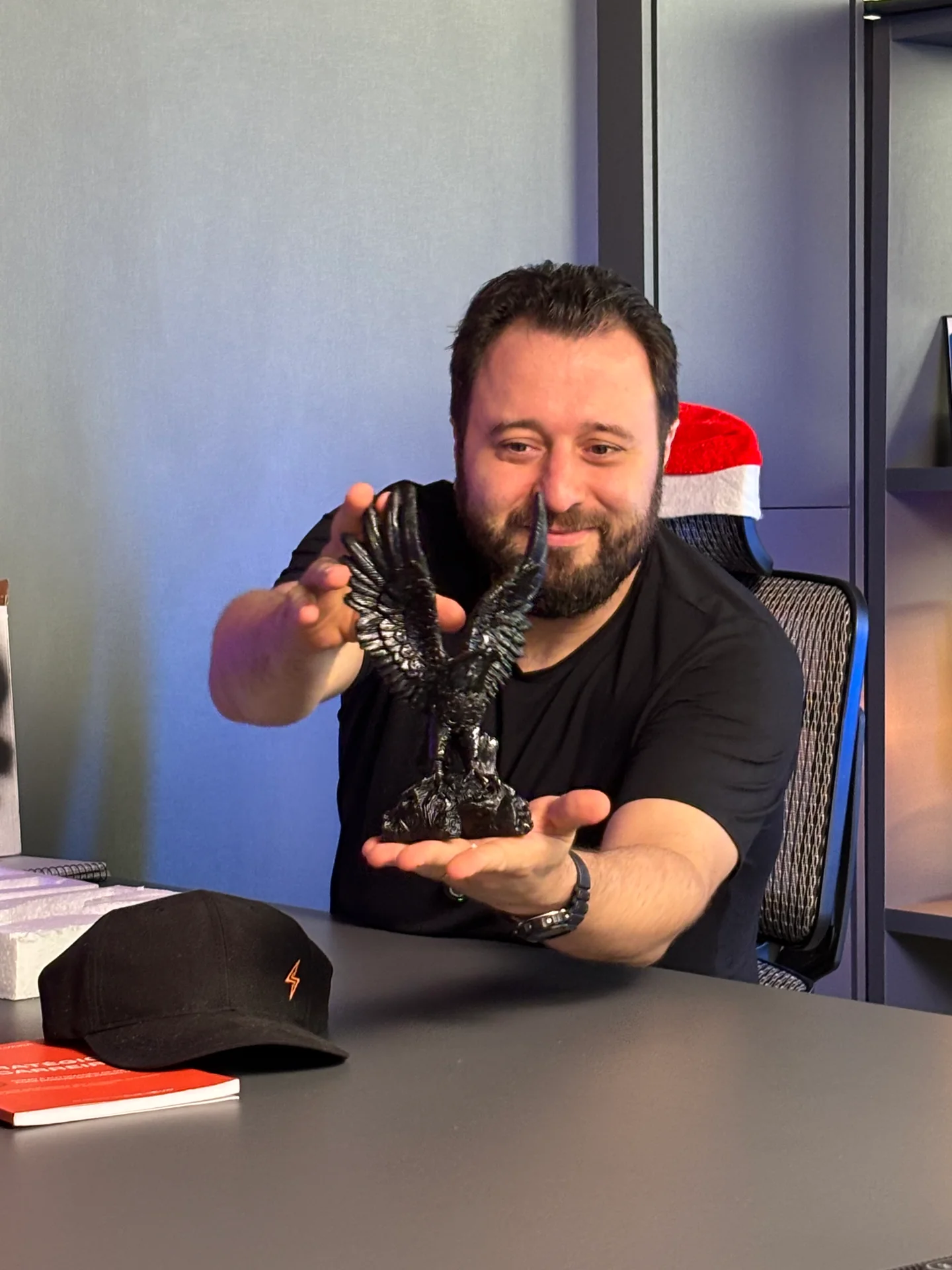 Joviano à mesa do estúdio, segurando uma escultura de águia.